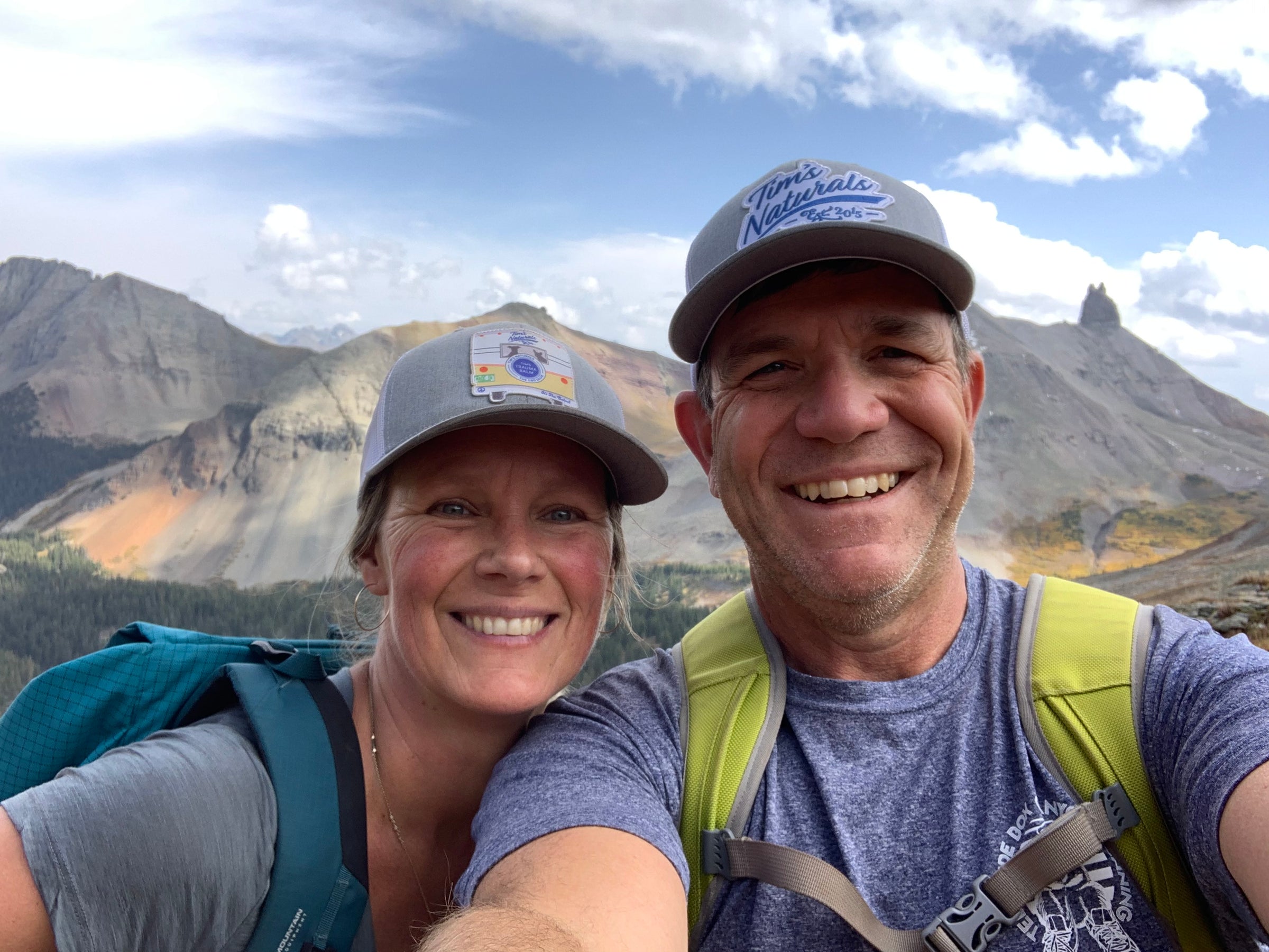 tim lafferty and jenny chicanski smiling at the camera with Tim's Naturals hatss on and mountains in the background