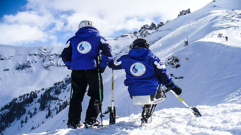 Telluride adaptive sports ski instructor and para-athlete in ski chair at the top of a snowy ski trail with blue sky and clouds beyond