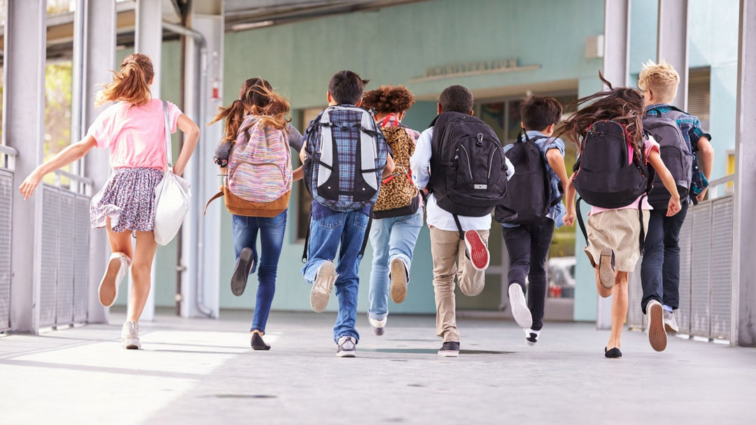 Eight kids running away from the camera with backpacks on, white floor and light green backdrop
