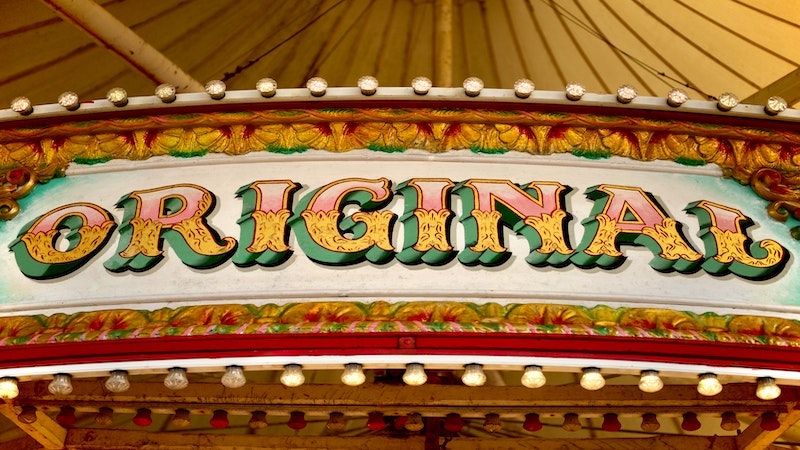 Original in western font written in green, yellow and pink on a marquee sign with yellow and red filigree and marquee lights.