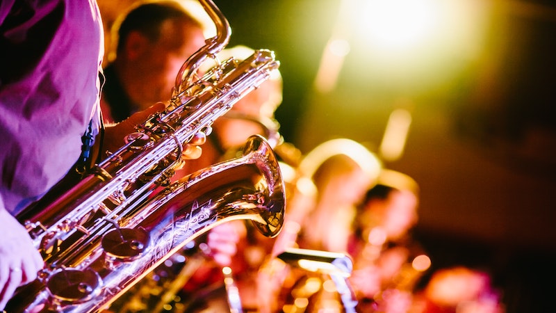 Saxophone reflecting purple light, with musicians lined up playing other brass instruments in the background