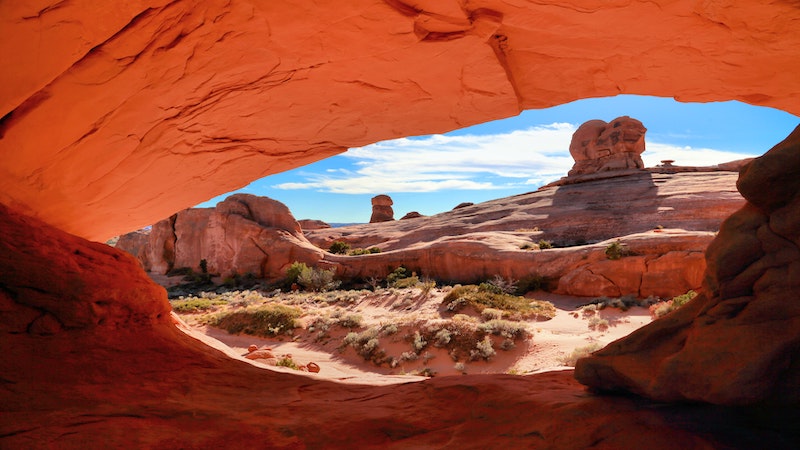 Blue Sky, cloudss, Red Rocks arches and towers seen through a red rock arch