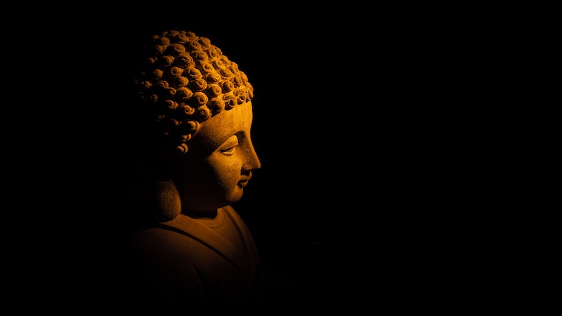 Golden buddha statue bust shadowed in black background